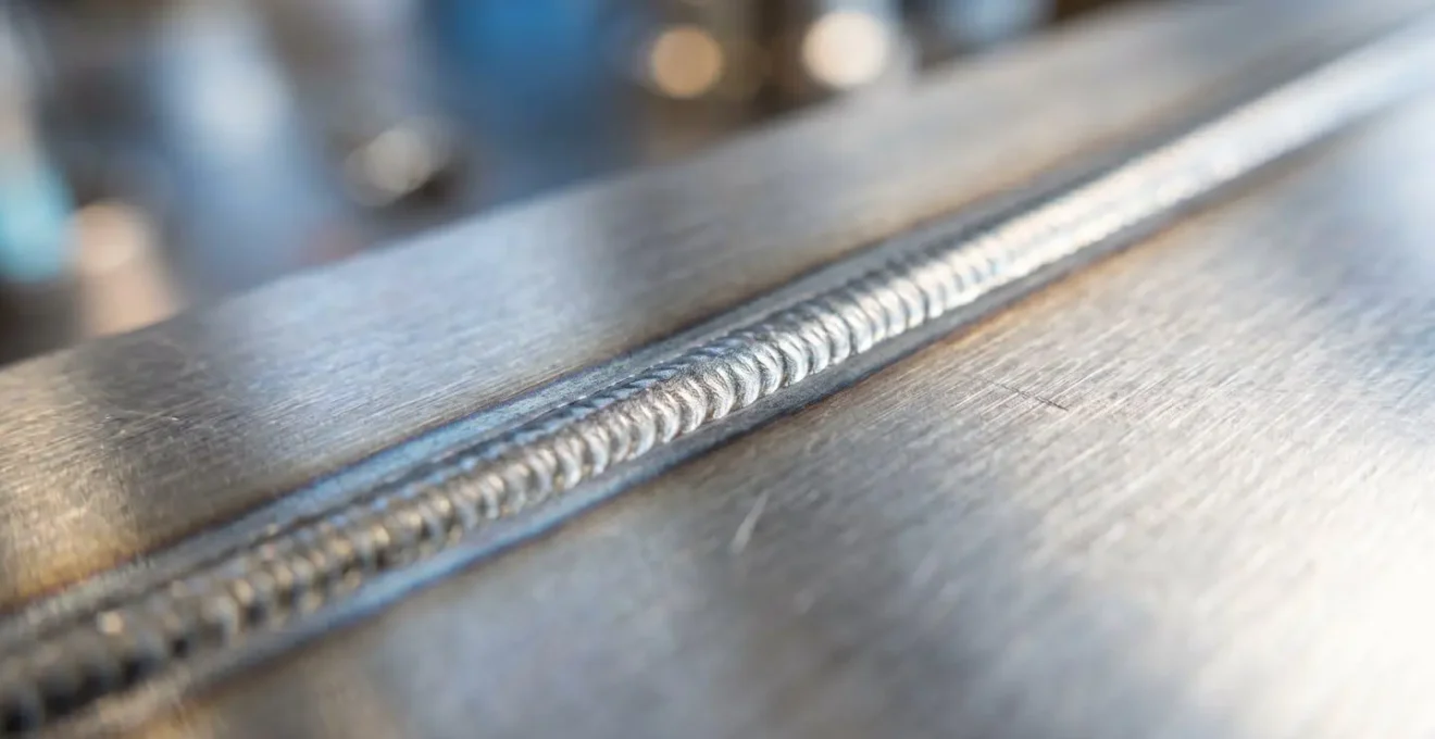 Vue en gros plan d'un cordon de soudure laser parfaitement régulier sur une tôle d'acier inoxydable brillante